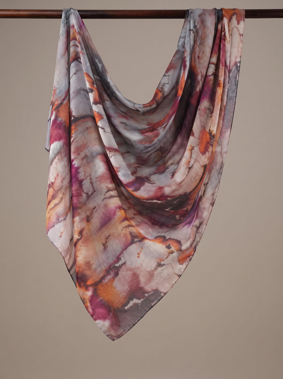 A lightweight square scarf with an abstract marbled pattern in shades of orange, purple, pink, and gray, draped over a dark wooden hanger against a solid beige background.